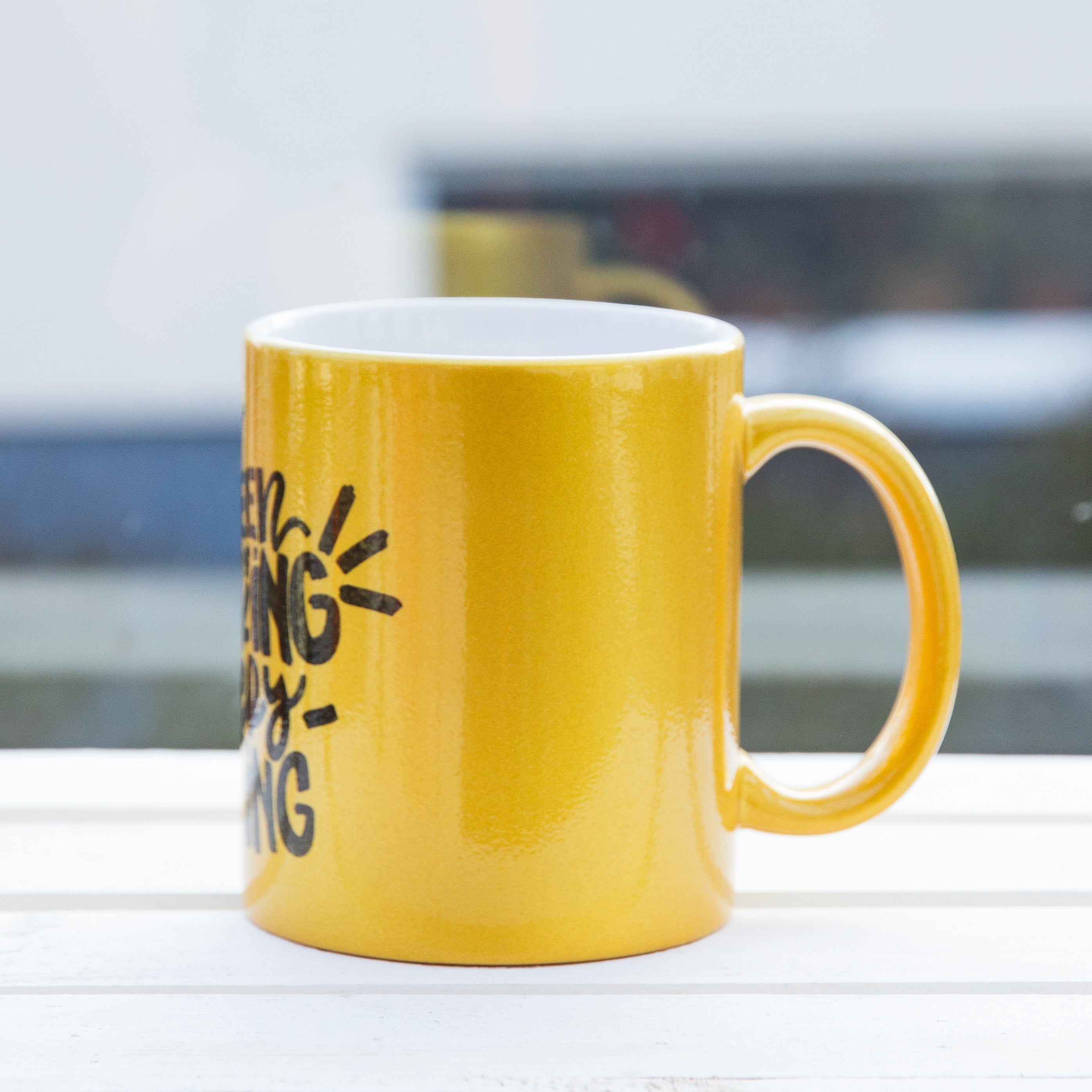 linke Seiten Ansicht einer goldenen Tasse mit Druck der Henkel zeigt nach rechts