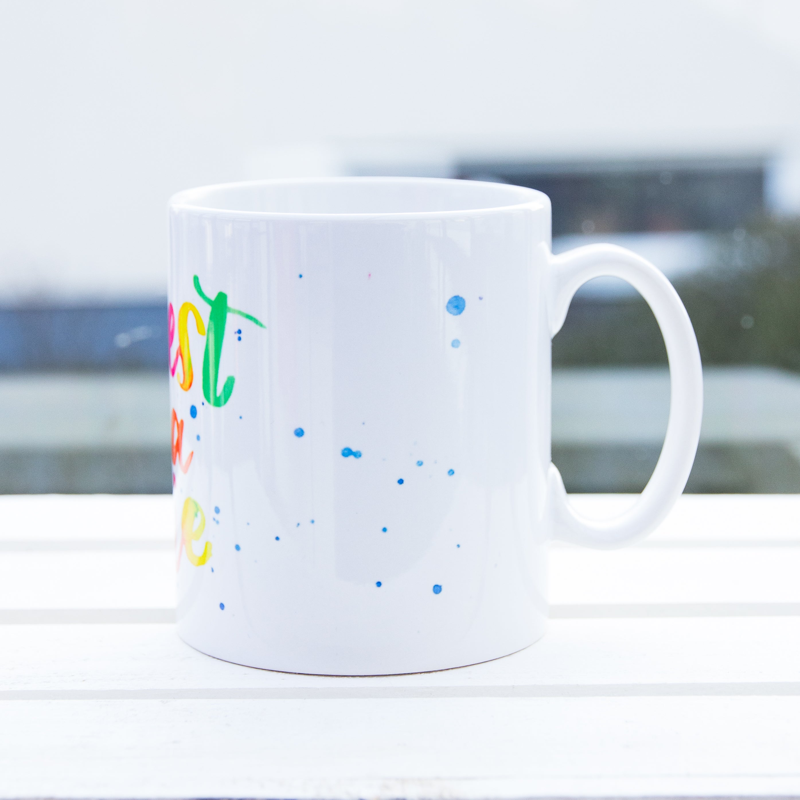 linke Seiten Ansicht einer weißen Tasse mit Aufdruck C'est la vie der Henkel zeigt nach rechts
